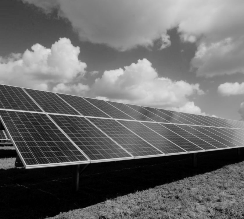Large array of ground-mounted solar panels under a partly cloudy sky, showcasing renewable energy installation